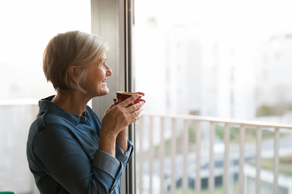 Older while woman sipping cup of coffee while looking out the window